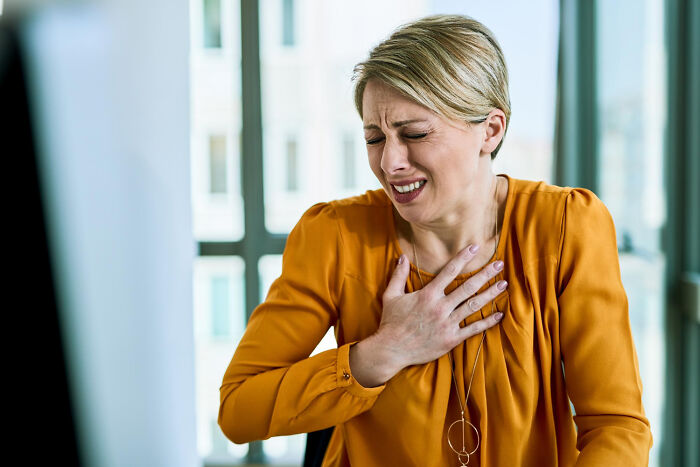 Woman in an orange blouse clutching her chest in pain, illustrating terrifying medical conditions with no symptoms.