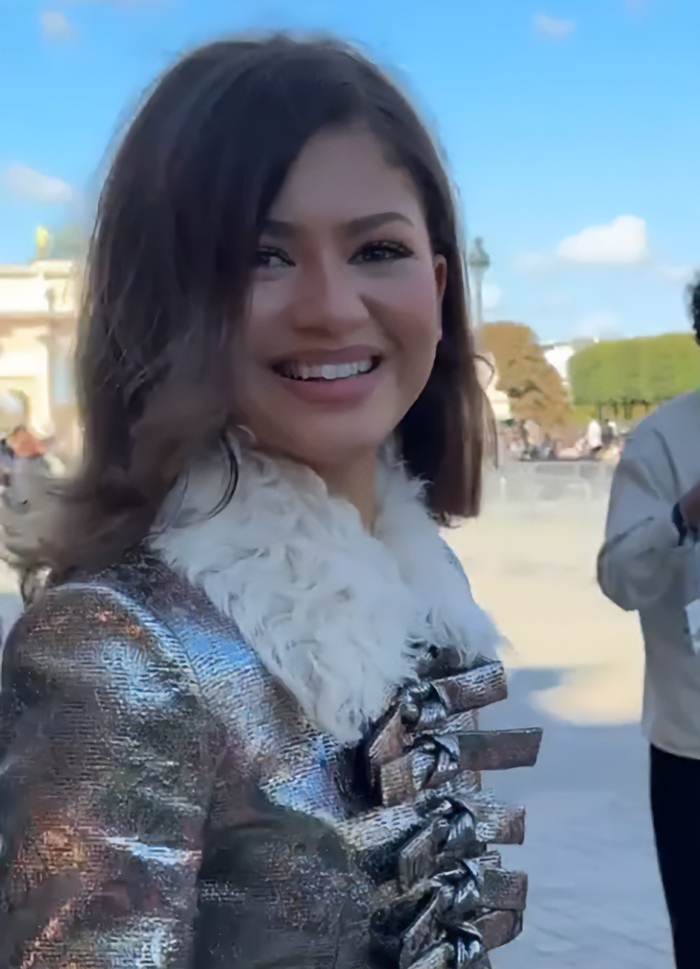 Zendaya smiling outdoors wearing a metallic coat with fur collar, sparking fans' speculation about her pregnancy.