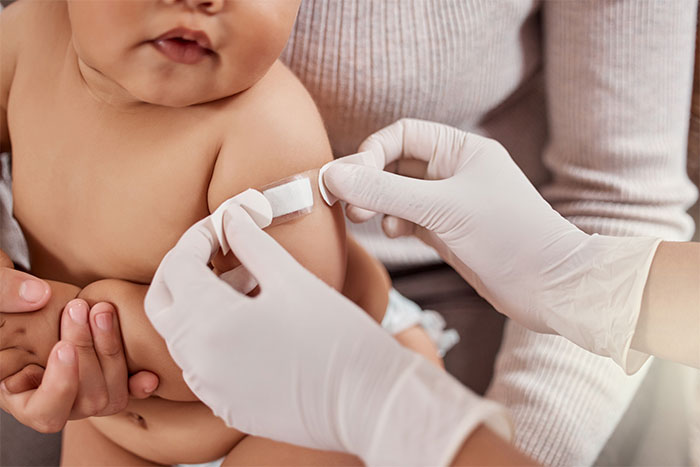 A baby receiving a vaccination with a healthcare worker applying a bandage on the child's arm after the shot.