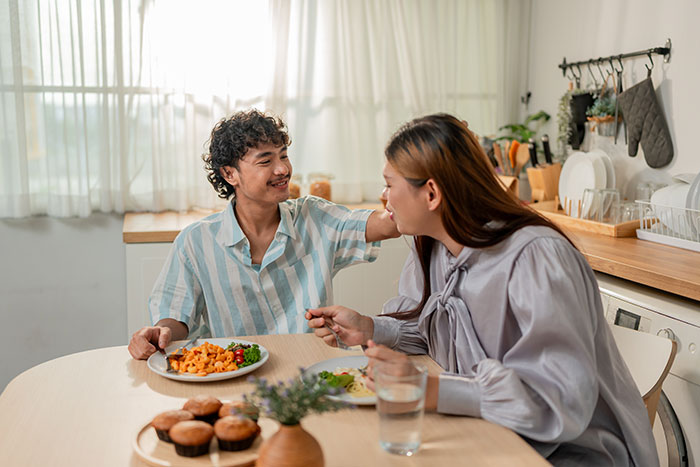 Couple having a tense conversation at the kitchen table highlighting issues of wife hears husband admit ugly woman.