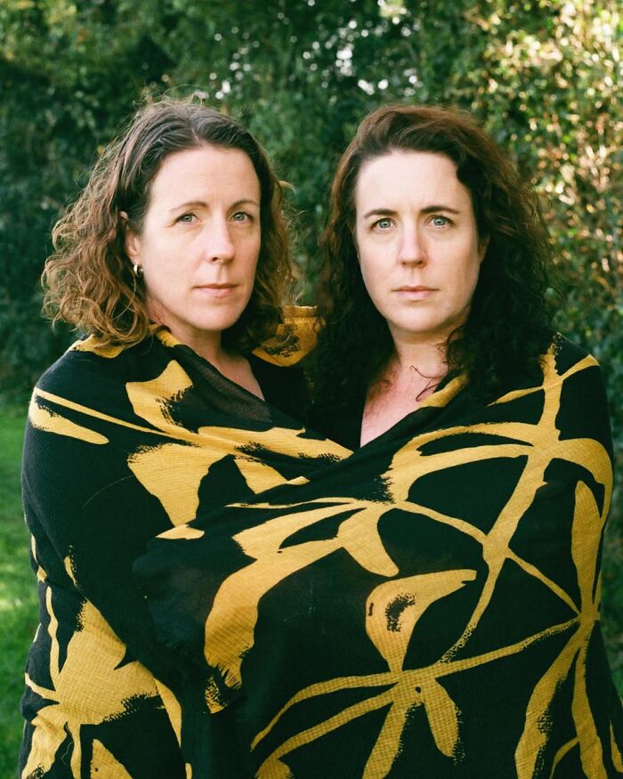 Twin sisters wrapped in a patterned blanket standing outdoors, captured by a London photographer in a stunning portrait.