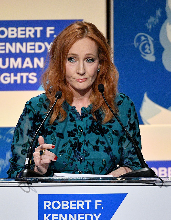 J.K. Rowling speaking at a podium during a Robert F. Kennedy Human Rights event with a serious expression.