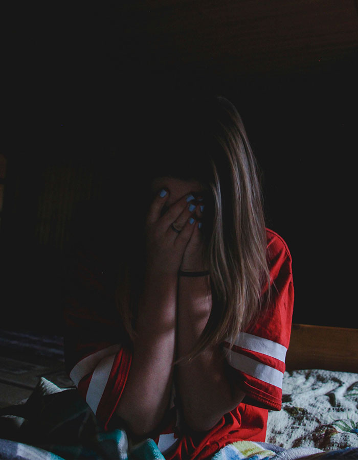 Teen girl covering her face in a dark room, conveying emotions of fear or distress related to pit bull protection story.