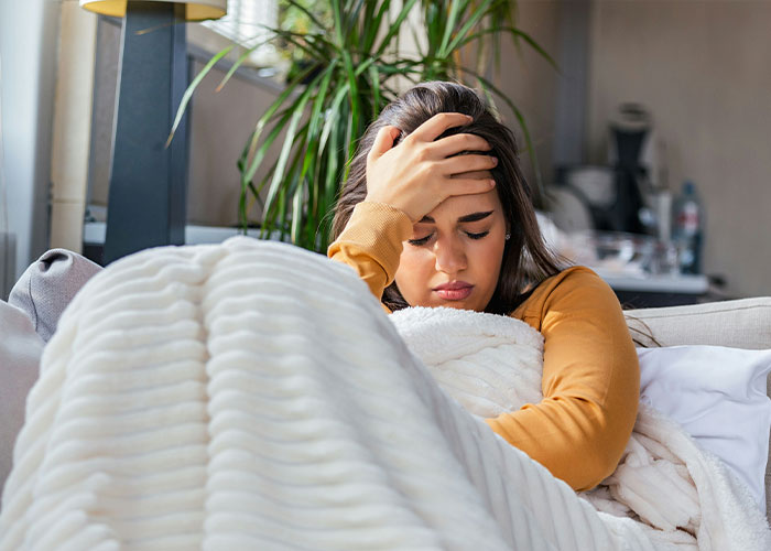 Woman looking unwell and resting with a white blanket, highlighting hidden dangers in common household items. Woman looking unwell and resting with a white blanket, highlighting hidden dangers in common household items.