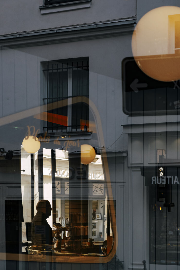 Silhouetted man inside a café, seen through reflective glass in a stunning street photography shot capturing unexpected moments.