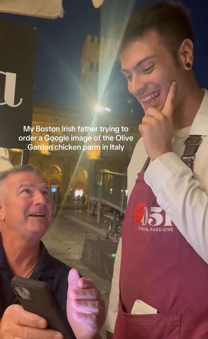 American tourist showing waiter a digital image of Olive Garden chicken parm in Italy, causing confusion and disgust.