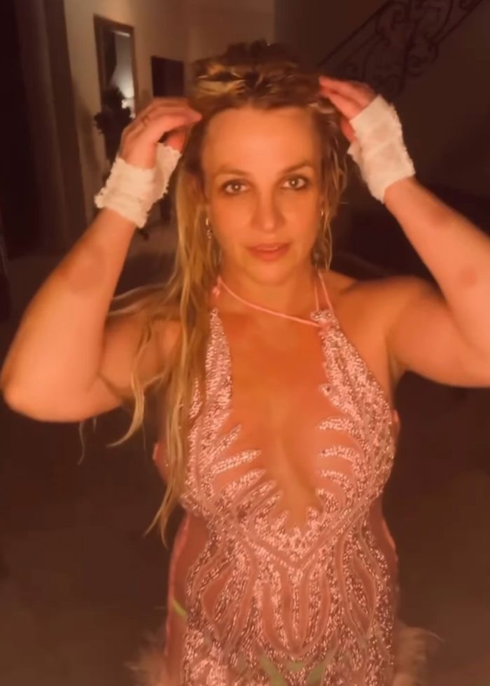 Britney Spears covering her bruised hands, making a concerning claim about a horrible accident in a dimly lit room.