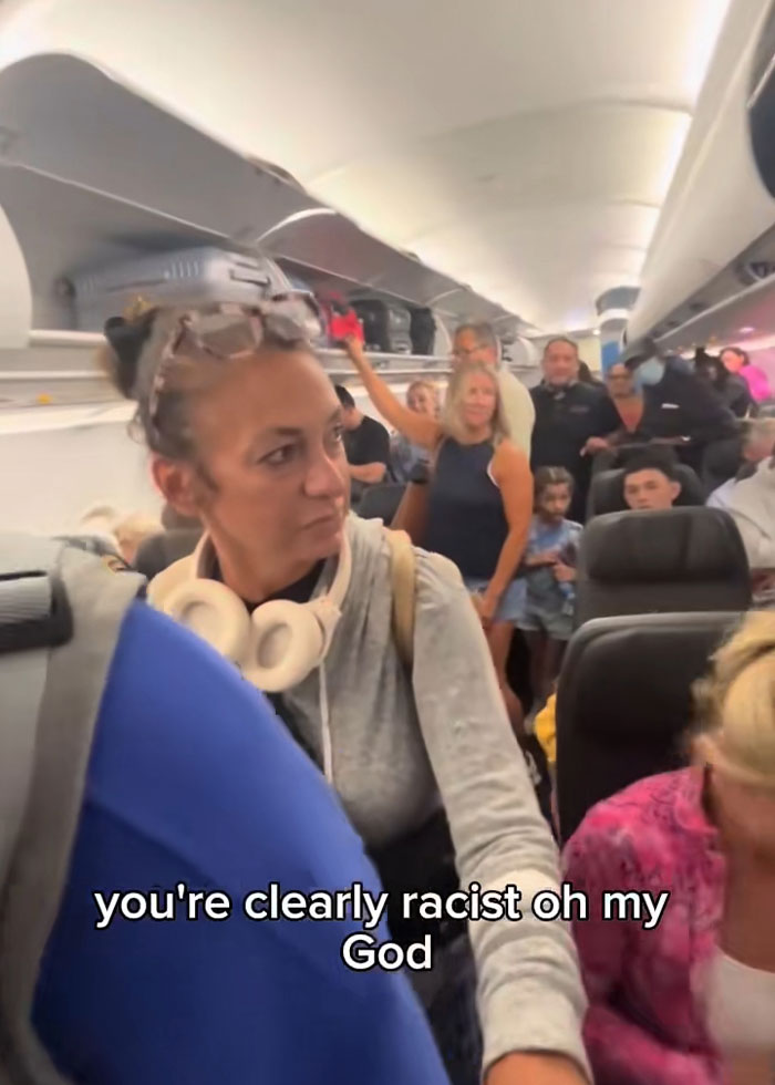 A woman, identified as Karen, arguing with multiple passengers on a crowded airplane during a heated incident. A woman, identified as Karen, arguing with multiple passengers on a crowded airplane during a heated incident.