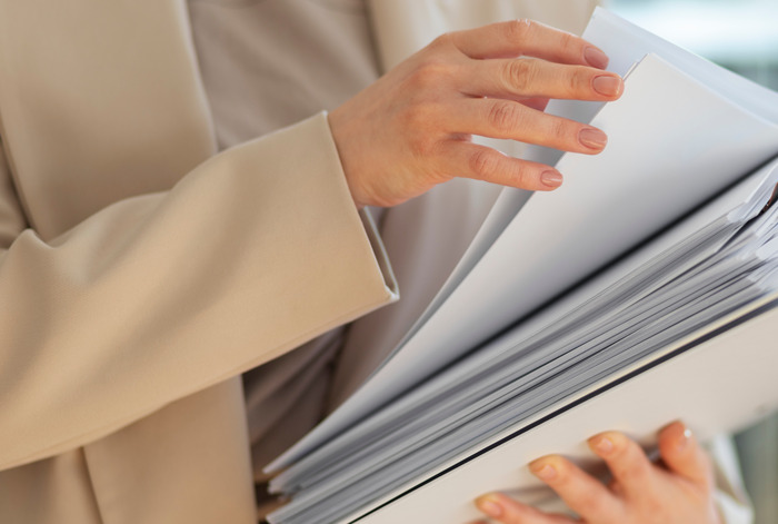 Person in beige blazer holding a thick stack of documents, representing unexpected work situations and awkward moments.