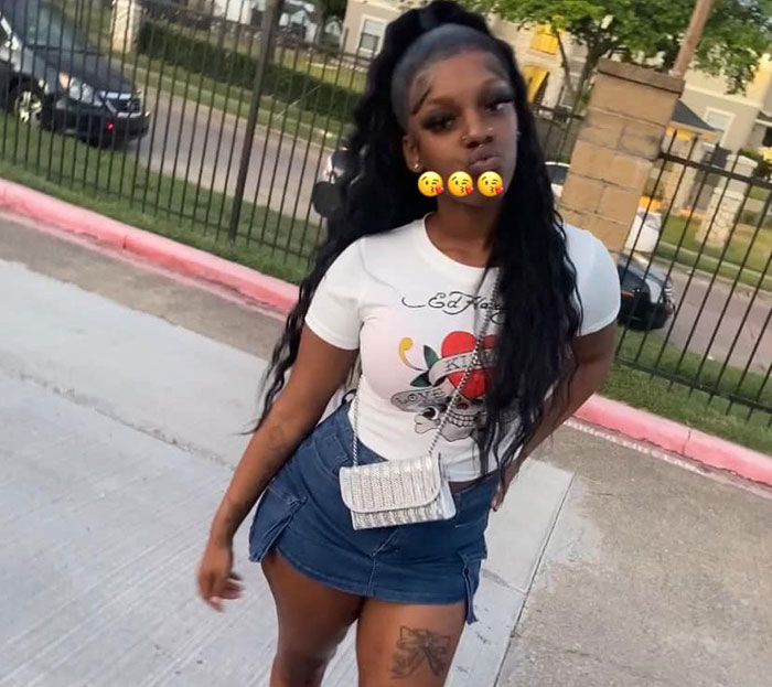 Young woman standing outside near a pet store, wearing a white graphic tee and denim skirt, showing casual style.