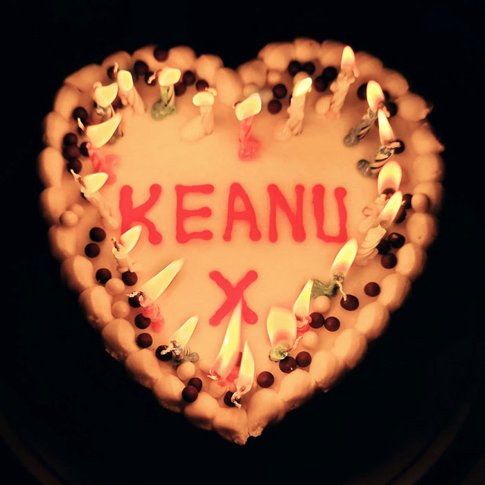 Heart-shaped cake with lit candles and Keanu written in red icing, related to Keanu Reeves marriage rumors.