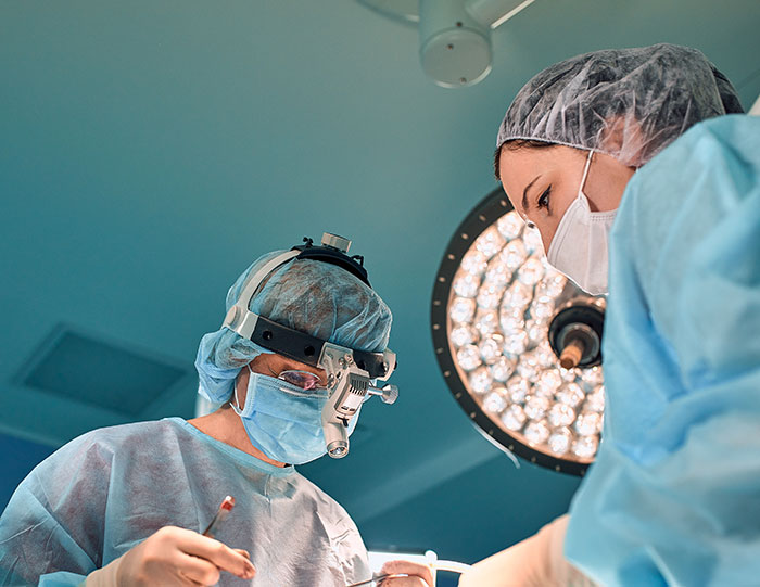 Brain surgeon and assistant performing delicate operation under surgical lights in a sterile operating room.