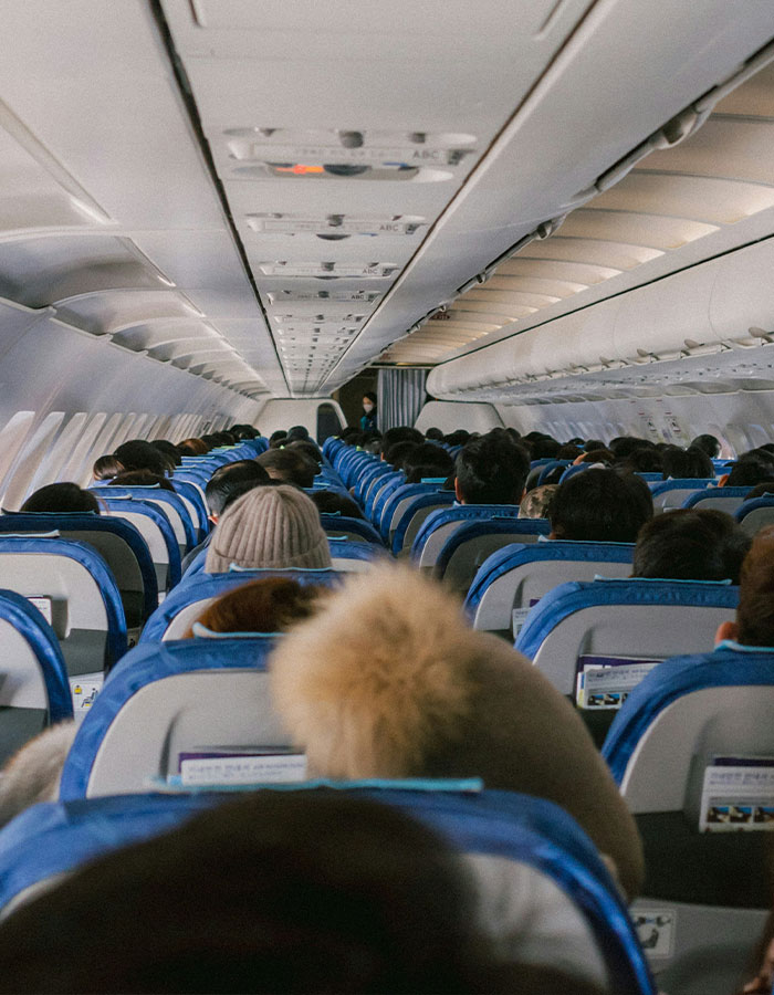 Airplane interior with passengers seated mid-flight, setting for confrontation over husband's infidelity witnessed by furious wife.