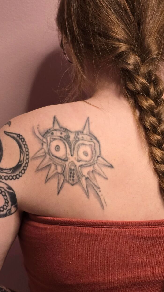 Tattoo of a spiked mask on a woman's shoulder with braided hair, showcasing one of the unusual tattoos allowed on bodies.