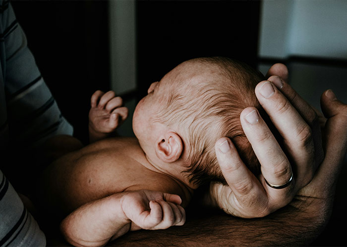 Newborn baby cradled gently in the hands of a 16-year-old dad, highlighting tender care despite difficult circumstances.