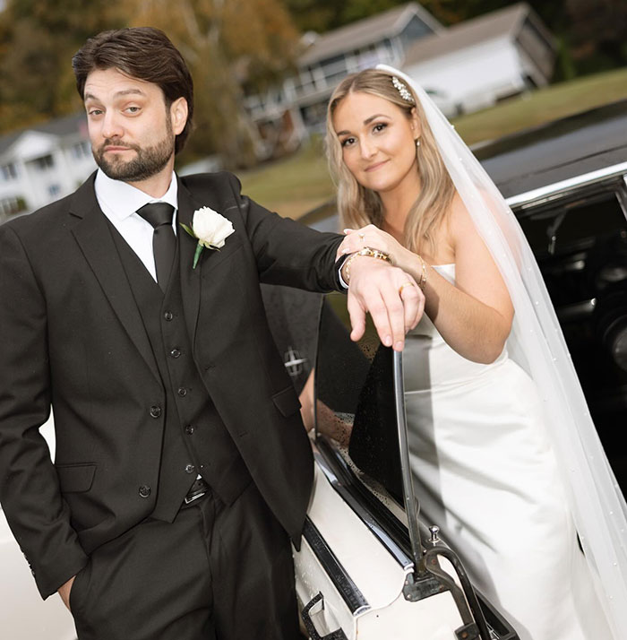 Bride and groom posing by a car on their wedding day, related to officials revealing cause of couple passing.