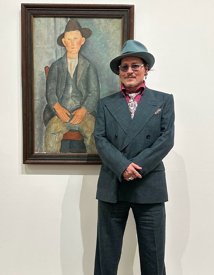 Johnny Depp in a suit and hat standing next to a framed painting, related to Johnny Depp&rsquo;s new movie role backlash.