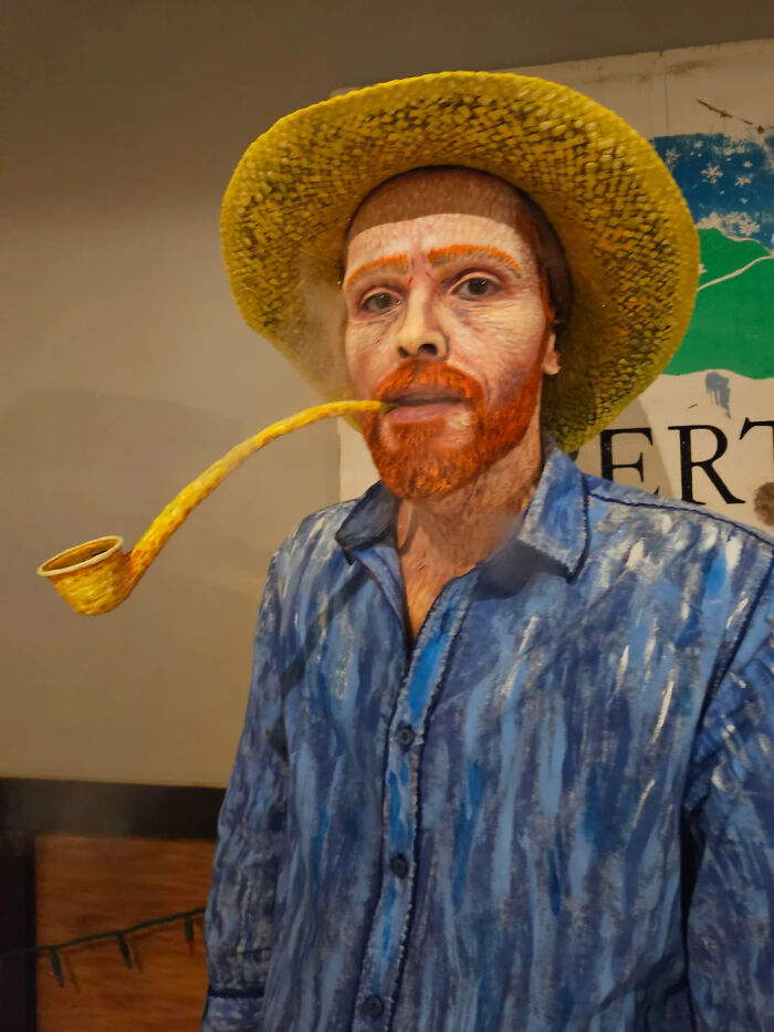 Artist dressed as Vincent van Gogh with detailed makeup, hand-painted costume, yellow hat, and smoking a long pipe.
