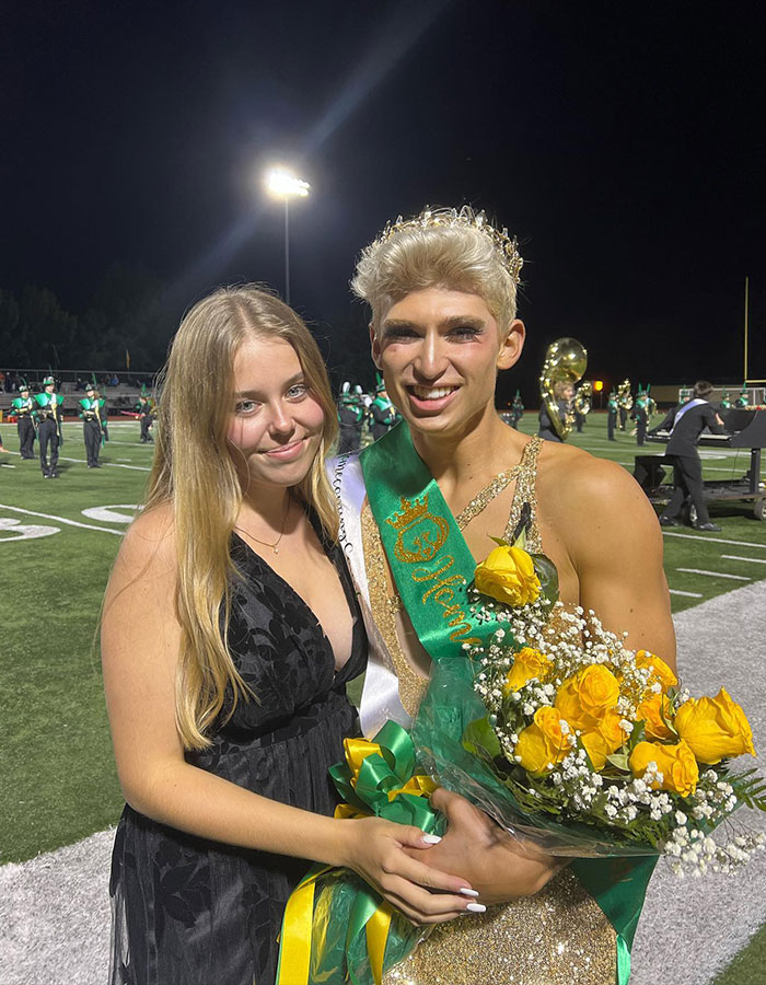 Missouri&rsquo;s first male homecoming queen wearing crown and sash, holding yellow roses, standing with a young woman on football field.