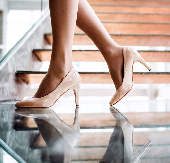 Woman wearing beige high heels walking on reflective glass floor by wooden stairs showing one-in-a-million coincidences concept