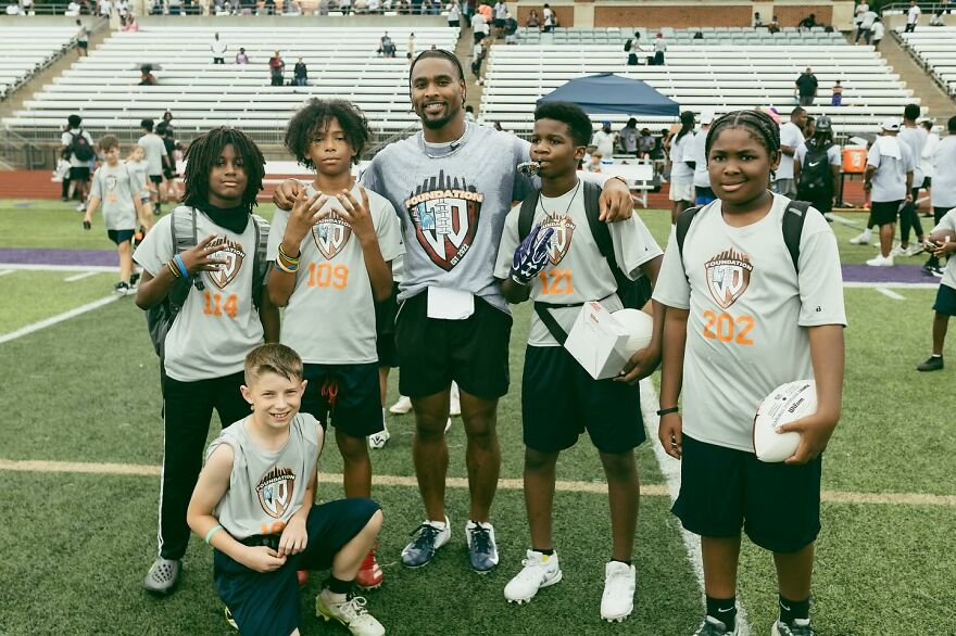 Jonathan Owens posing with kids on football field wearing foundation shirts in a community sports event. Jonathan Owens posing with kids on football field wearing foundation shirts in a community sports event.