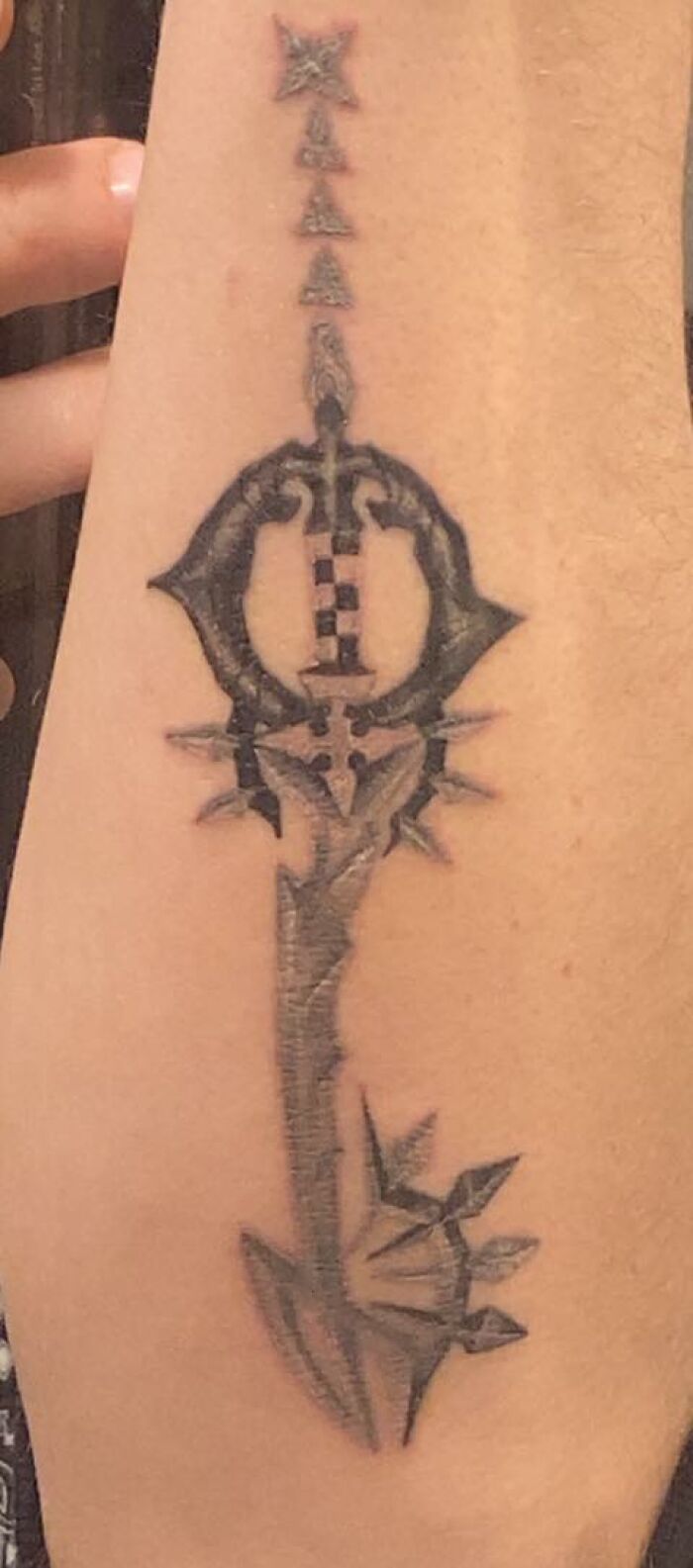 Black and gray abstract tattoo with arrow and star elements on a person's forearm, unusual body tattoo design.