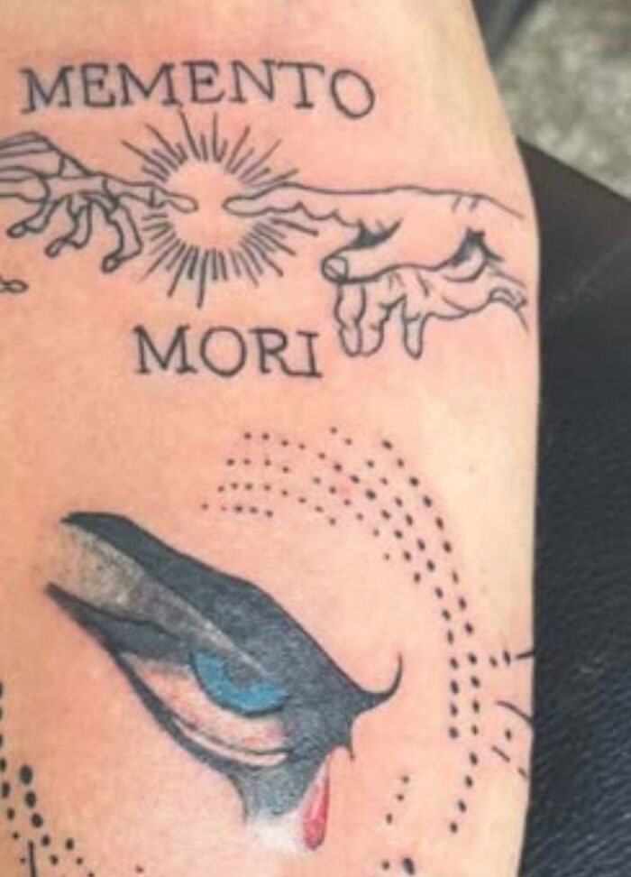Tattoo on skin featuring Memento Mori text and artistic hands with a detailed eye design below, unique tattoo art.
