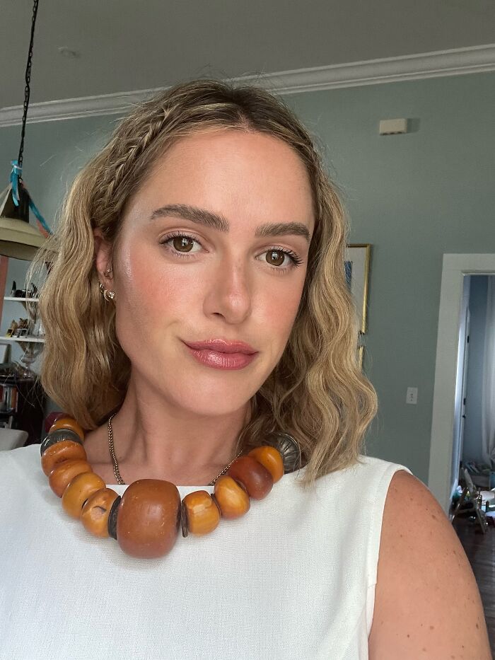 Young woman indoors wearing a chunky brown bead necklace, related to mystery woman at center of cheating rumors revealed.