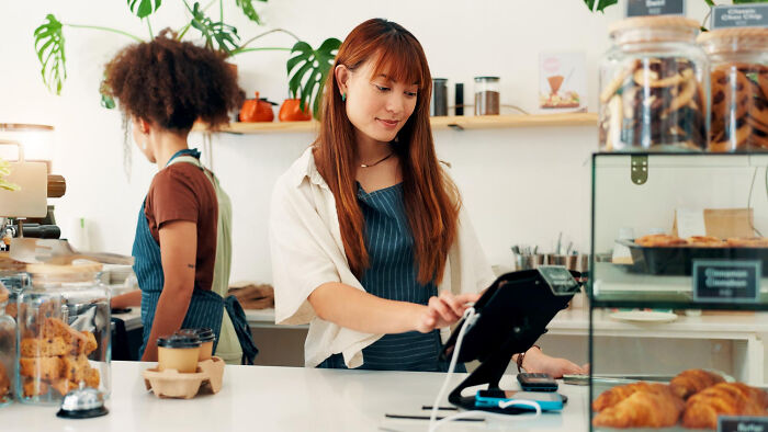 Two restaurant staff working behind the counter handling orders and payments in a cozy café setting.