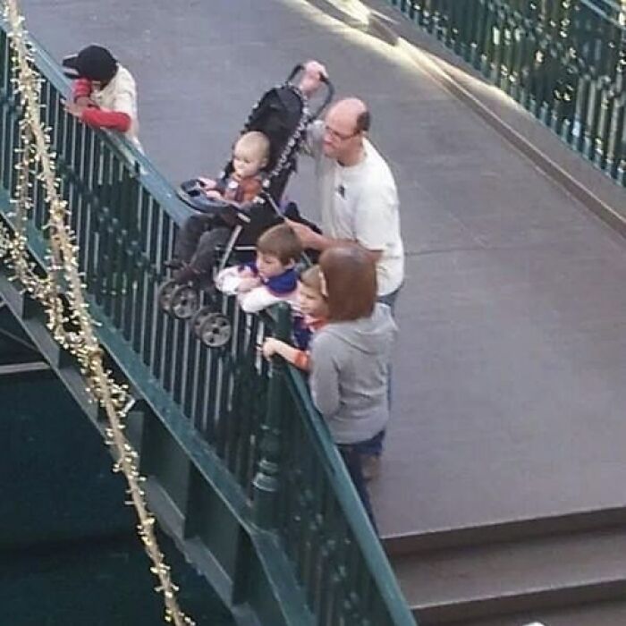 Family with children gathered on a bridge railing in a risky position, an image that might need a priest or exorcist.