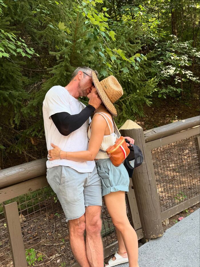 Couple kissing outdoors by wooden fence and trees, related to Kristen Bell wedding anniversary post triggering victims.