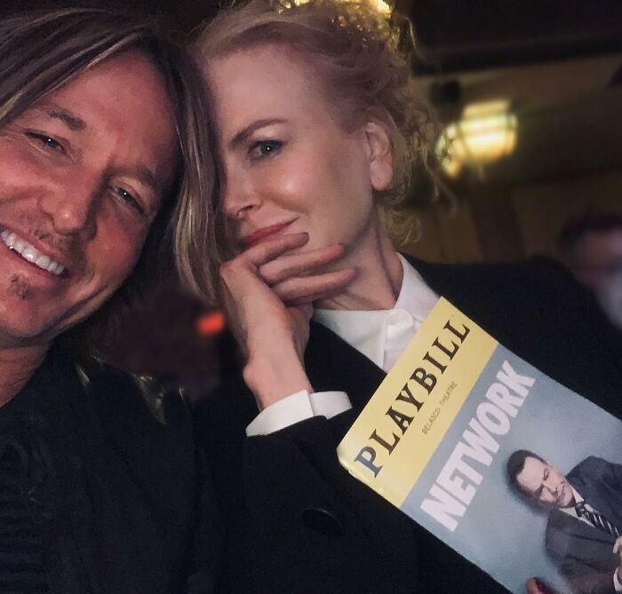 Nicole Kidman and Keith Urban smiling together, Nicole holding a Playbill for Network in a dimly lit setting.