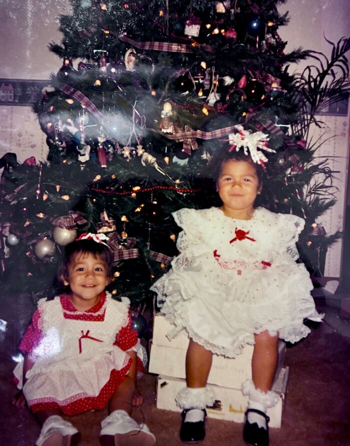 Two young sisters in festive dresses sitting by a decorated Christmas tree, a miracle discovery after 36 years missing.