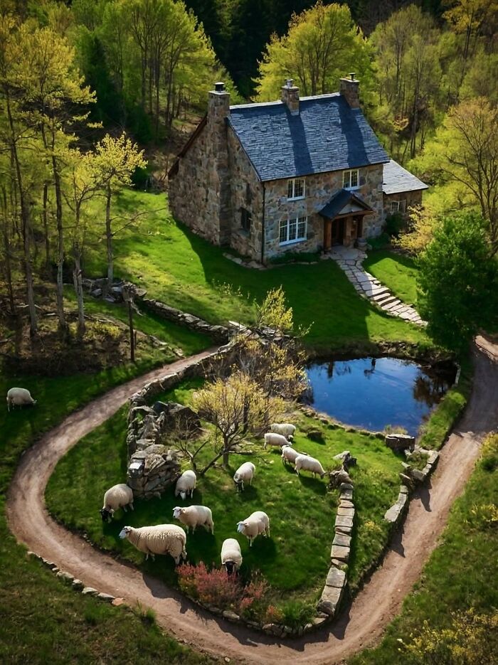 Stone cottage surrounded by gardens, sheep grazing near a pond, and lush greenery in an idyllic countryside setting.