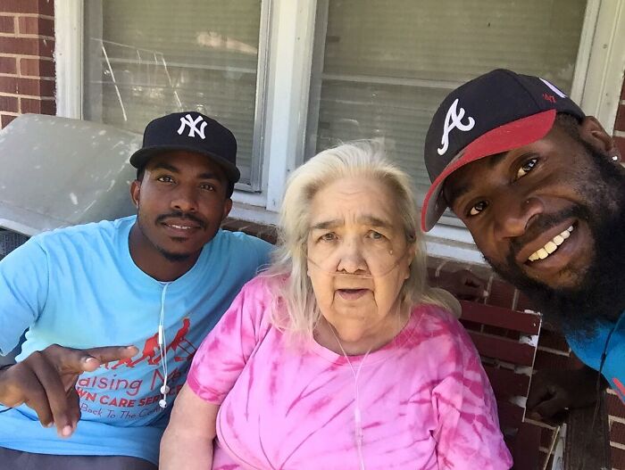 Two men smiling with an elderly woman on a porch, showing faith in humanity restored through kindness of strangers.