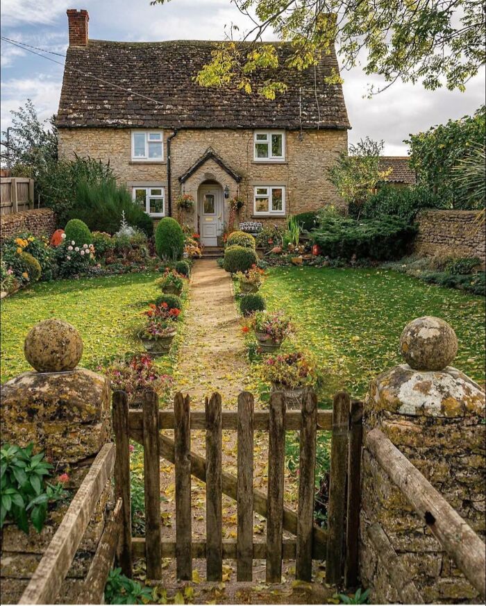 Charming stone cottage with a lush garden and wooden gate, embodying idyllic dream cottages and gardens in a peaceful setting.