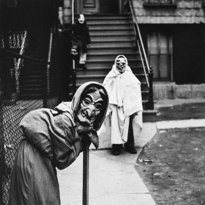 Vintage Halloween costumes featuring eerie masks and cloaks on children in a black and white urban setting.