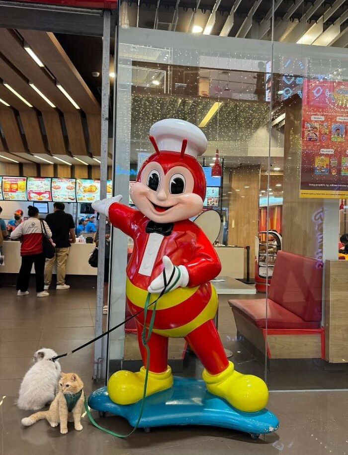 Mascot statue holding leashes of two small animals, showcasing wholesome animal comedy in a lighthearted setting.