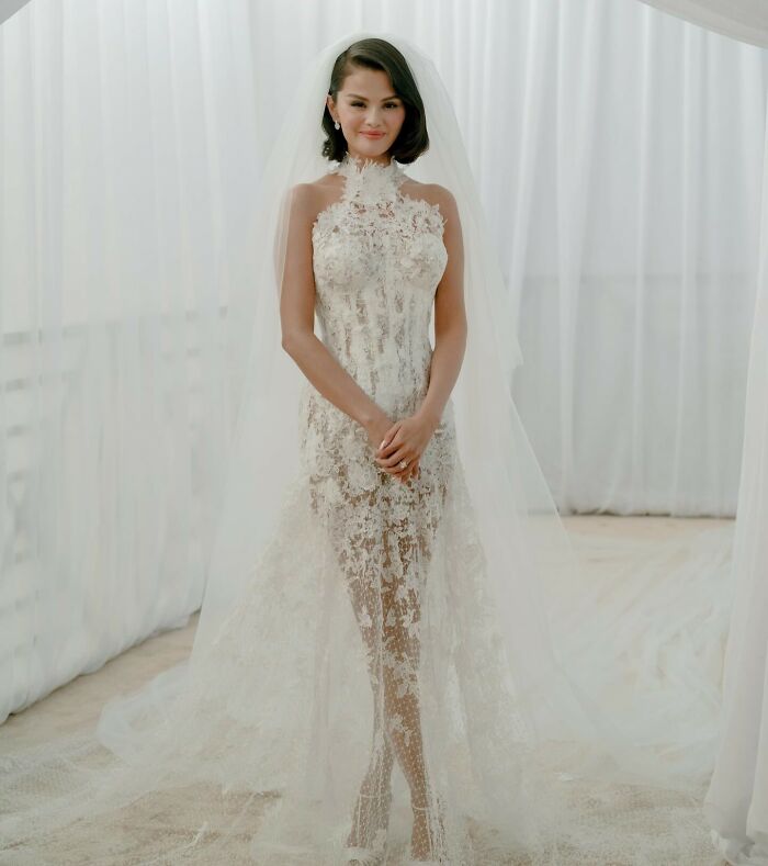 Selena Gomez in a lace wedding dress and veil, posing gracefully amid fans suspicious of her kidney donor and wedding drama.