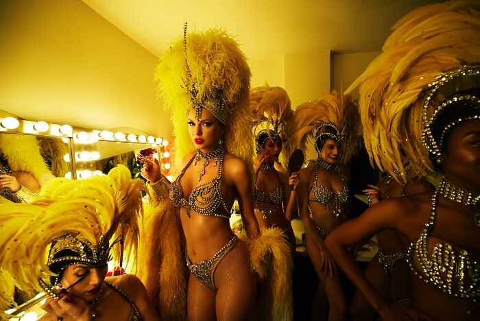 Showgirls in elaborate yellow feather costumes backstage, capturing the vibrant and glamorous atmosphere of a performance.