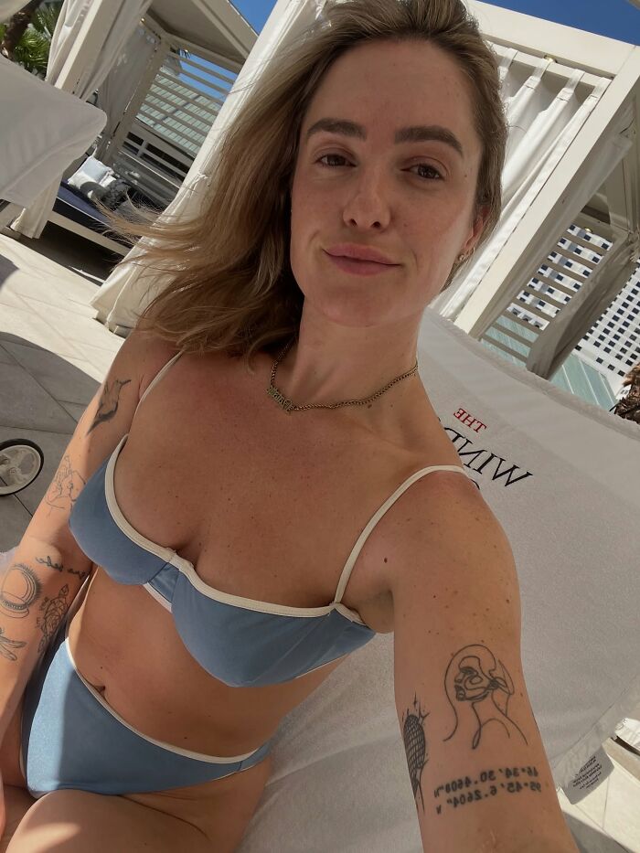 Woman in a blue bikini with tattoos relaxing by a pool, linked to Lily Allen and David Harbour cheating rumors mystery.