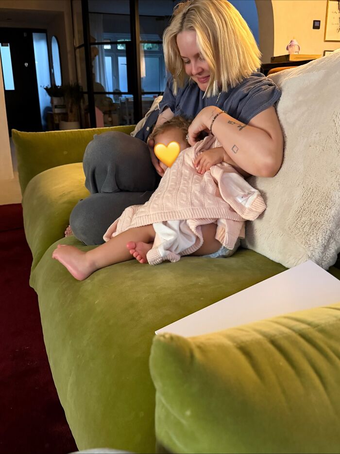 Pop star sitting on green couch, holding her baby wrapped in a pink blanket, sparking diabetes baby name discussion.
