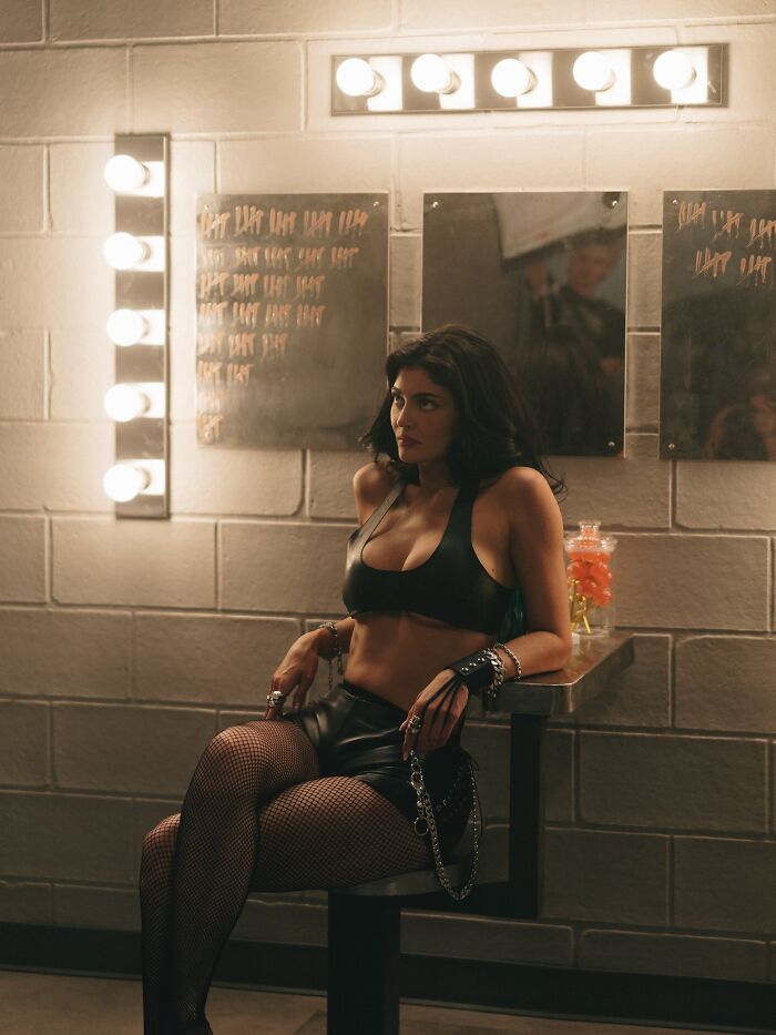 Kylie Jenner sitting in leather outfit with fishnet stockings in a dressing room amid fake arrest video controversy.