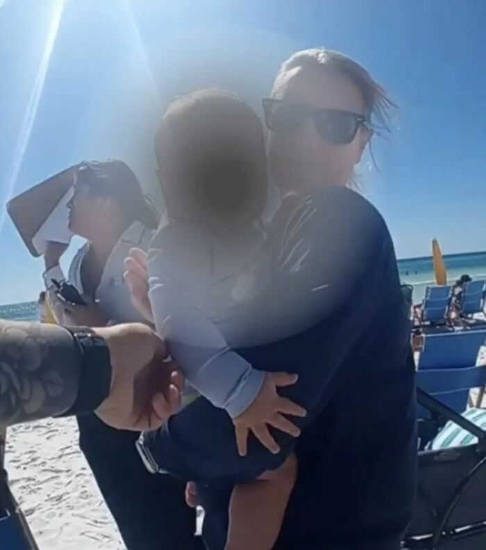 Healthcare exec holding baby on beach with people and umbrellas in background on a sunny day related to child safety concern. Healthcare exec holding baby on beach with people and umbrellas in background on a sunny day related to child safety concern.