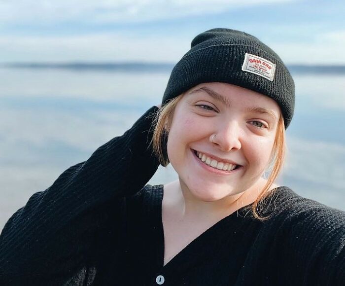 Young woman wearing a black beanie smiling outdoors by the water, related to music festival accident and Post Malone.