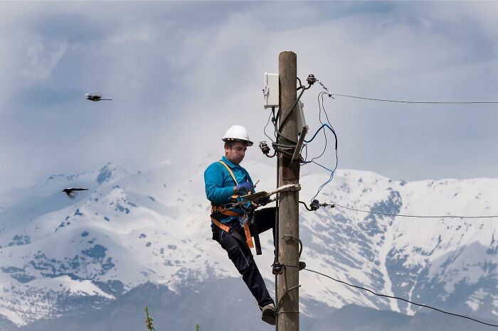 Electrician wearing safety gear working on a utility pole with snowy mountains in the background, life on Istanbul’s streets.
