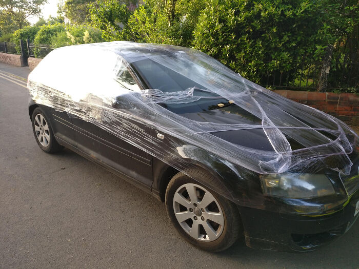Black car wrapped in plastic wrap as an example of petty revenge on a residential street.