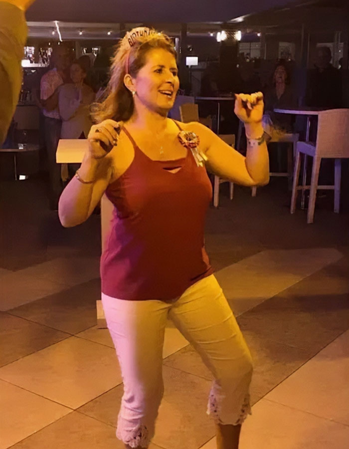 Woman smiling and dancing at a party, celebrating life with a funny obituary she wrote herself.