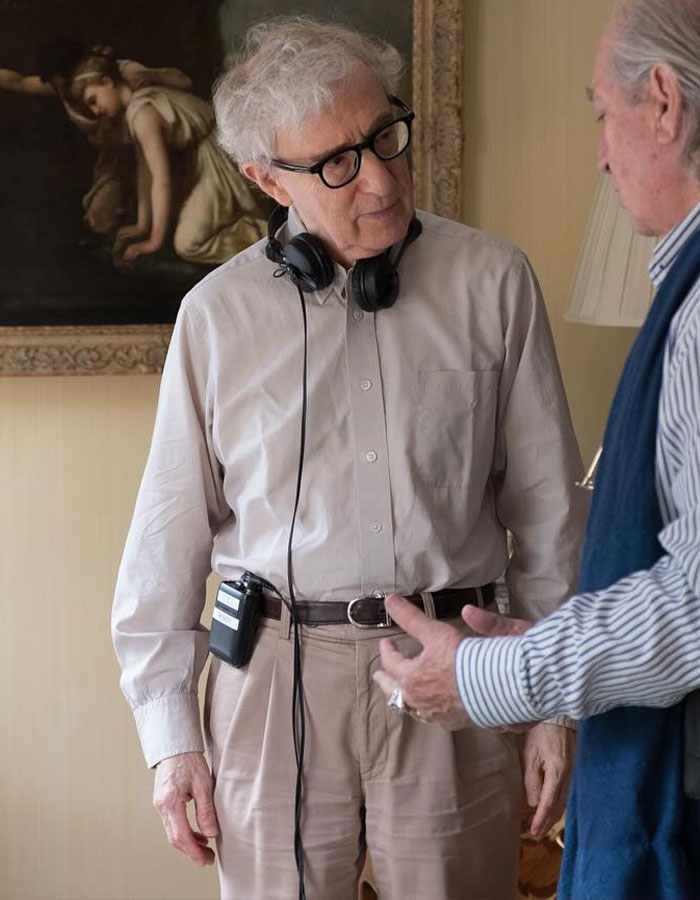 Older man with headphones around his neck talking with another man indoors, illustrating famous men shorter than fans imagined.