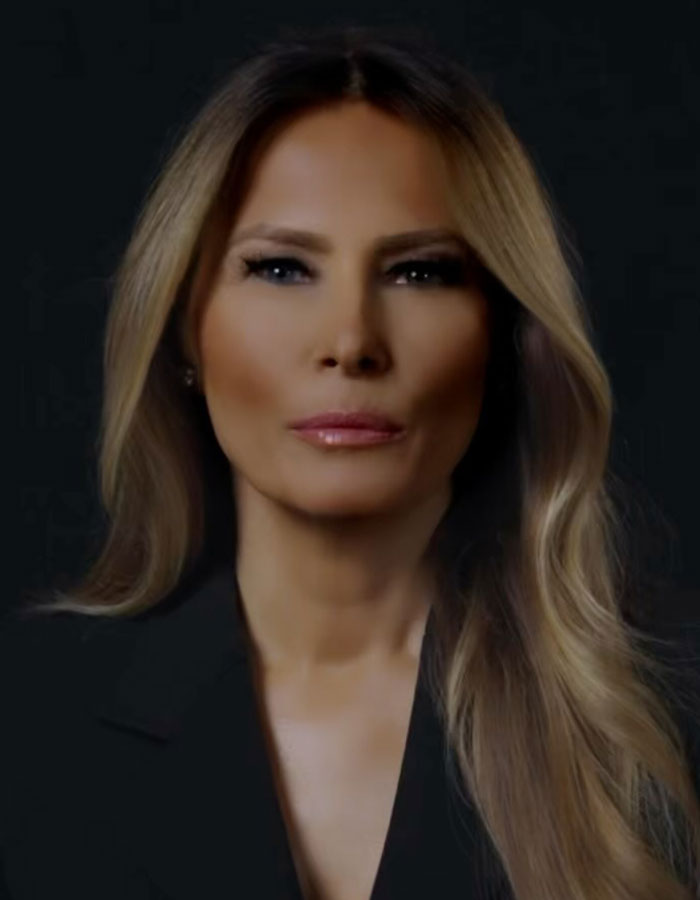Melania Trump in a stylized AI video, with serious expression and long blonde hair against a black background.